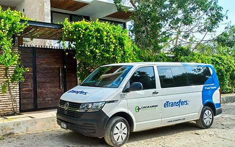 Fotografía de una van de transporte de pasajeros del aeropuerto de Cancún con el logotipo de eTransfers aparcada frente a un hotel.